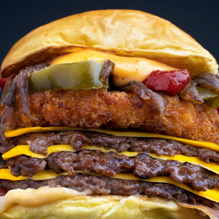 Close-up of a tall cheeseburger with a crispy fried patty, melted cheddar, pickles, onions, and a soft bun.