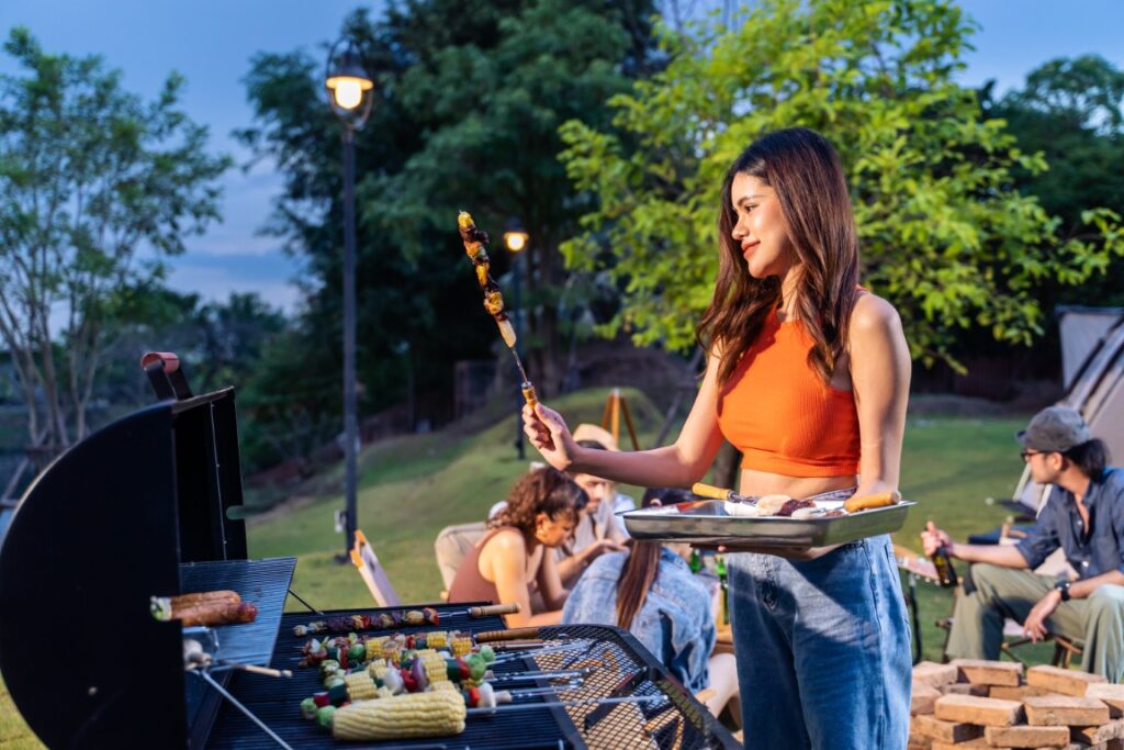SBBlood Pressure 1 Woman in an orange top grills skewers at a backyard barbecue while friends relax on the lawn at dusk.
