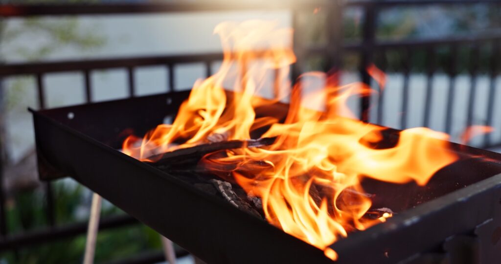 Flames lick a metal barbecue grill filled with burning charcoal on a deck.