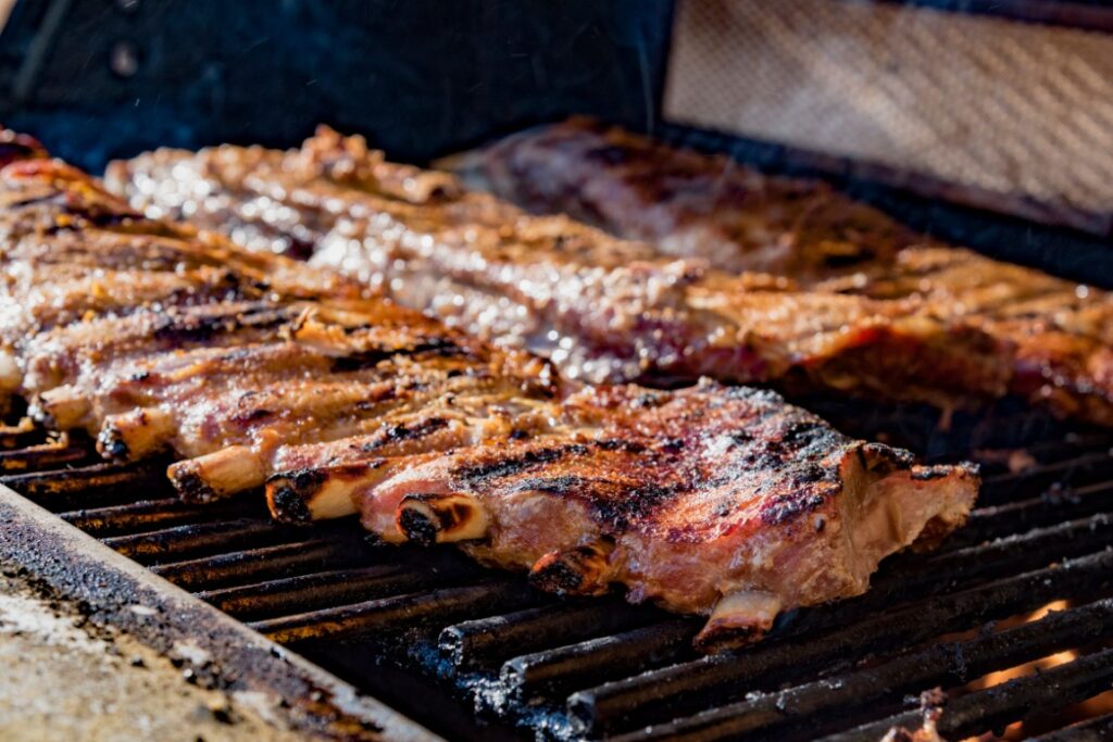 Pork ribs cooking on a charcoal grill with sizzling juices and charred edges over open flames