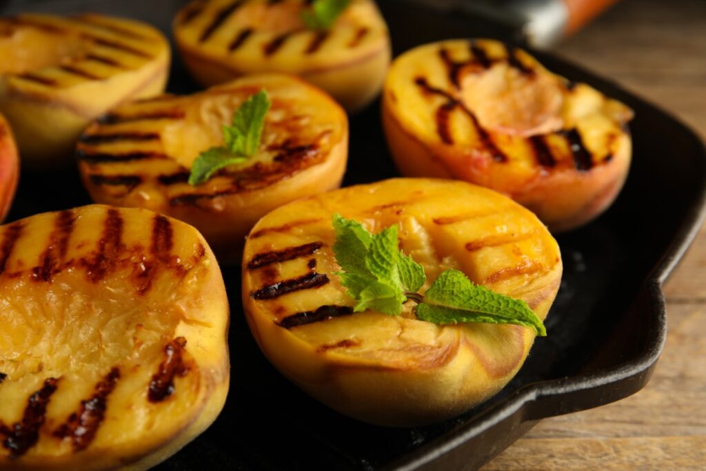 Grilled peach halves with mint leaves on a cast-iron skillet, showing caramelized grill marks.