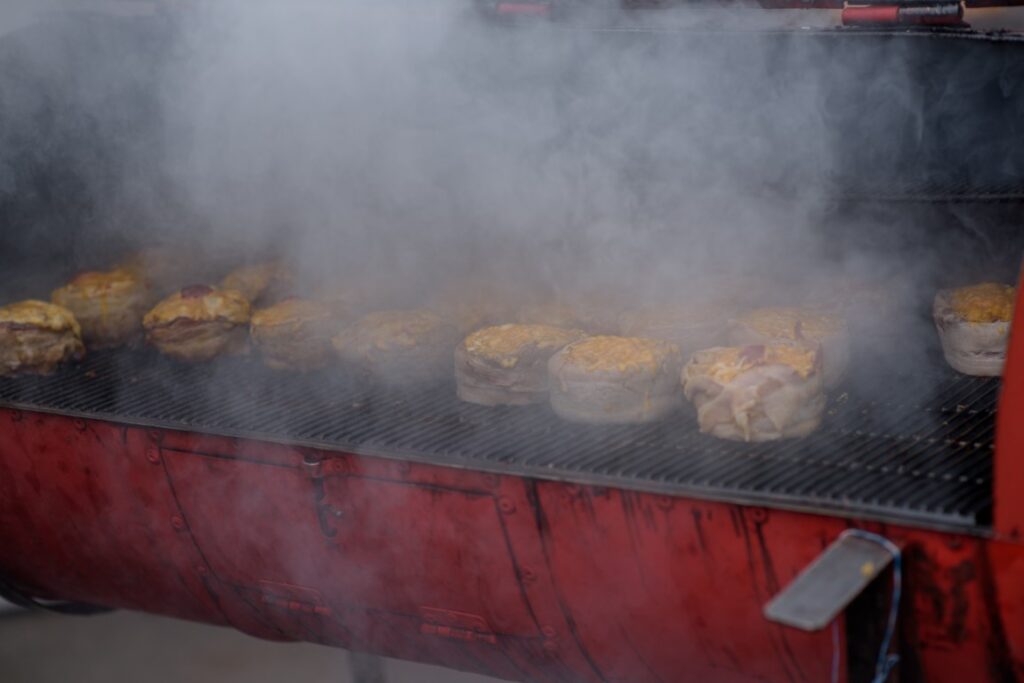 Barbecue grill with several burgers cooking on a smoky grill, red grill body visible at the bottom.