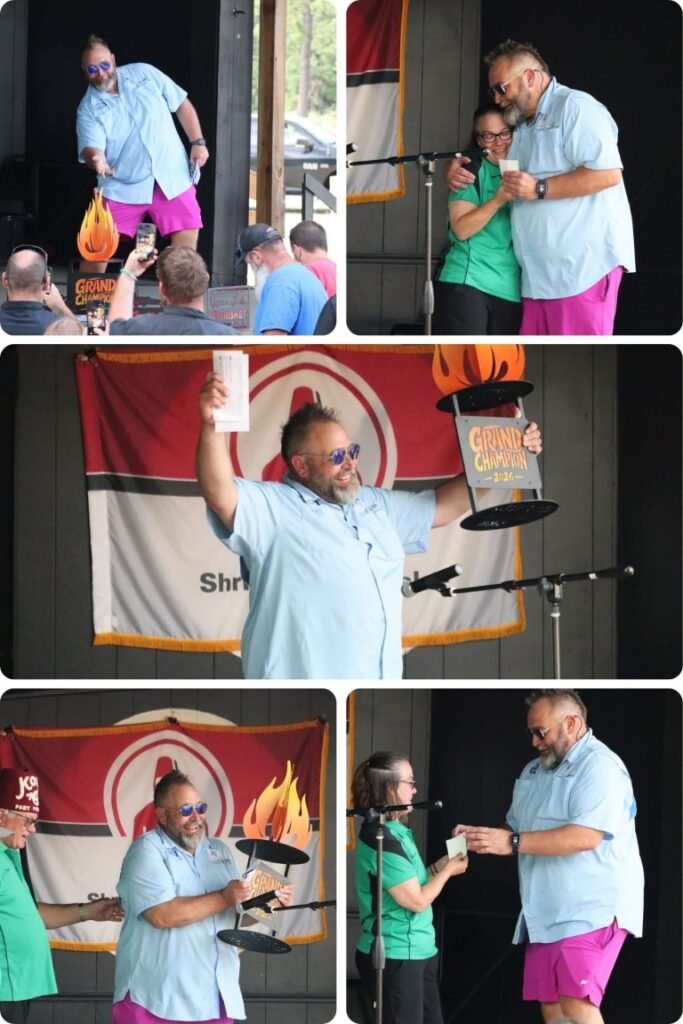 image009 Bearded man in a light blue shirt and pink shorts holds a flaming trophy on stage as the audience watches.