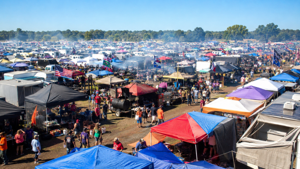 Smoke_Clears 5 - BBQ News Large outdoor tailgate/festival scene with hundreds of colorful tents, stalls, and attendees under a clear blue sky.